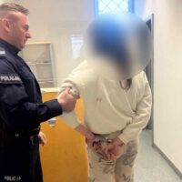 Policjant prowadzi zatrzymaną osobę korytarzem budynku policyjnego