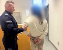 Policjant prowadzi zatrzymaną osobę korytarzem budynku policyjnego