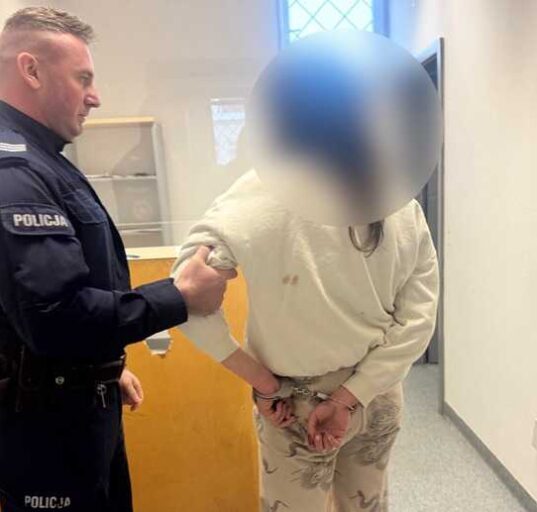 Policjant prowadzi zatrzymaną osobę korytarzem budynku policyjnego