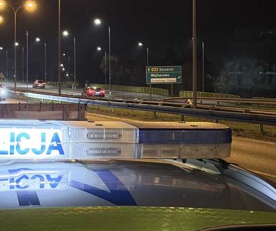 Policyjny radiowóz z włączoną belką świetlną „POLICJA” na tle nocnej drogi w okolicach Wejherowa