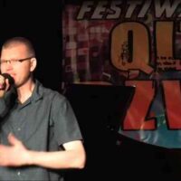 Przemysław Kamiński występuje na 11. edycji Festiwalu Qltury Dźwięku w Dębnie. Artysta śpiewa na scenie Domu Kultury przy ul. Daszyńskiego 20, prezentując utwór W Twoich oczach. W tle widoczne profesjonalne oświetlenie sceniczne i logotypy festiwalu.