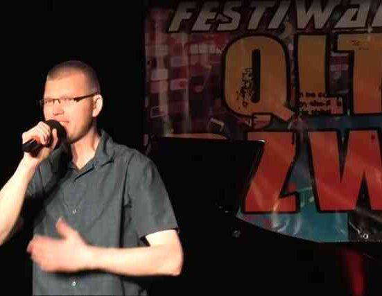 Przemysław Kamiński występuje na 11. edycji Festiwalu Qltury Dźwięku w Dębnie. Artysta śpiewa na scenie Domu Kultury przy ul. Daszyńskiego 20, prezentując utwór W Twoich oczach. W tle widoczne profesjonalne oświetlenie sceniczne i logotypy festiwalu.