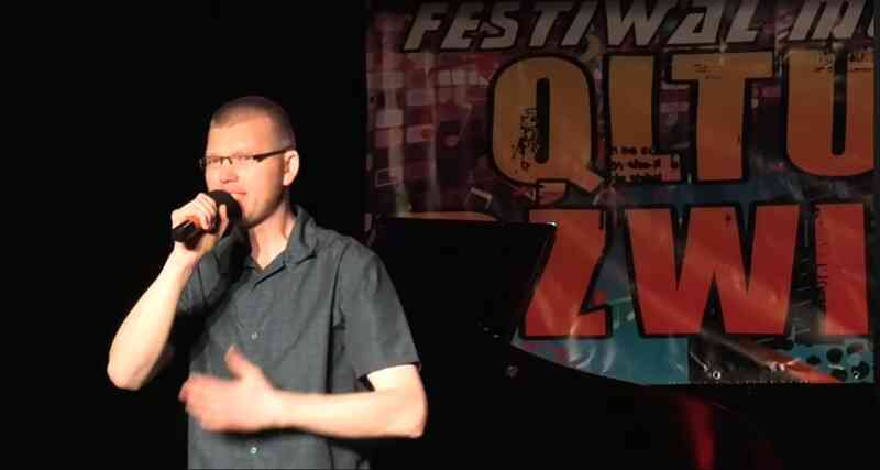 Przemysław Kamiński występuje na 11. edycji Festiwalu Qltury Dźwięku w Dębnie. Artysta śpiewa na scenie Domu Kultury przy ul. Daszyńskiego 20, prezentując utwór W Twoich oczach. W tle widoczne profesjonalne oświetlenie sceniczne i logotypy festiwalu.