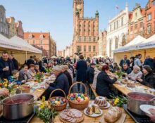 Grupa wolontariuszy serwująca gorący żurek z wielkiego kotła na Targu Węglowym w Gdańsku, w tle białe namioty i radosna atmosfera wspólnego posiłku.