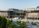 Widok z zewnątrz na Galerię Młociny w Warszawie z budynkiem centrum handlowego i strefą rekreacyjną