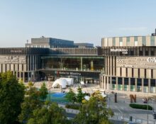 Widok z zewnątrz na Galerię Młociny w Warszawie z budynkiem centrum handlowego i strefą rekreacyjną