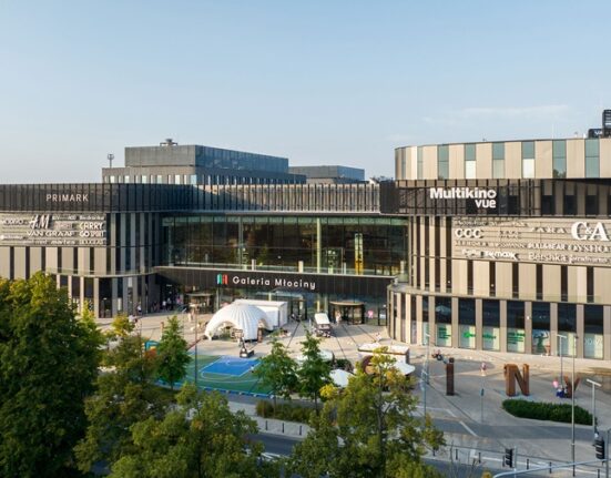 Widok z zewnątrz na Galerię Młociny w Warszawie z budynkiem centrum handlowego i strefą rekreacyjną