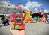 Pudełko słodyczy Wawel trzymane w dłoni przed kolorową ciężarówką Wawel Truck podczas wydarzenia plenerowego