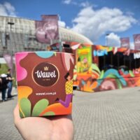 Pudełko słodyczy Wawel trzymane w dłoni przed kolorową ciężarówką Wawel Truck podczas wydarzenia plenerowego