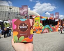 Pudełko słodyczy Wawel trzymane w dłoni przed kolorową ciężarówką Wawel Truck podczas wydarzenia plenerowego